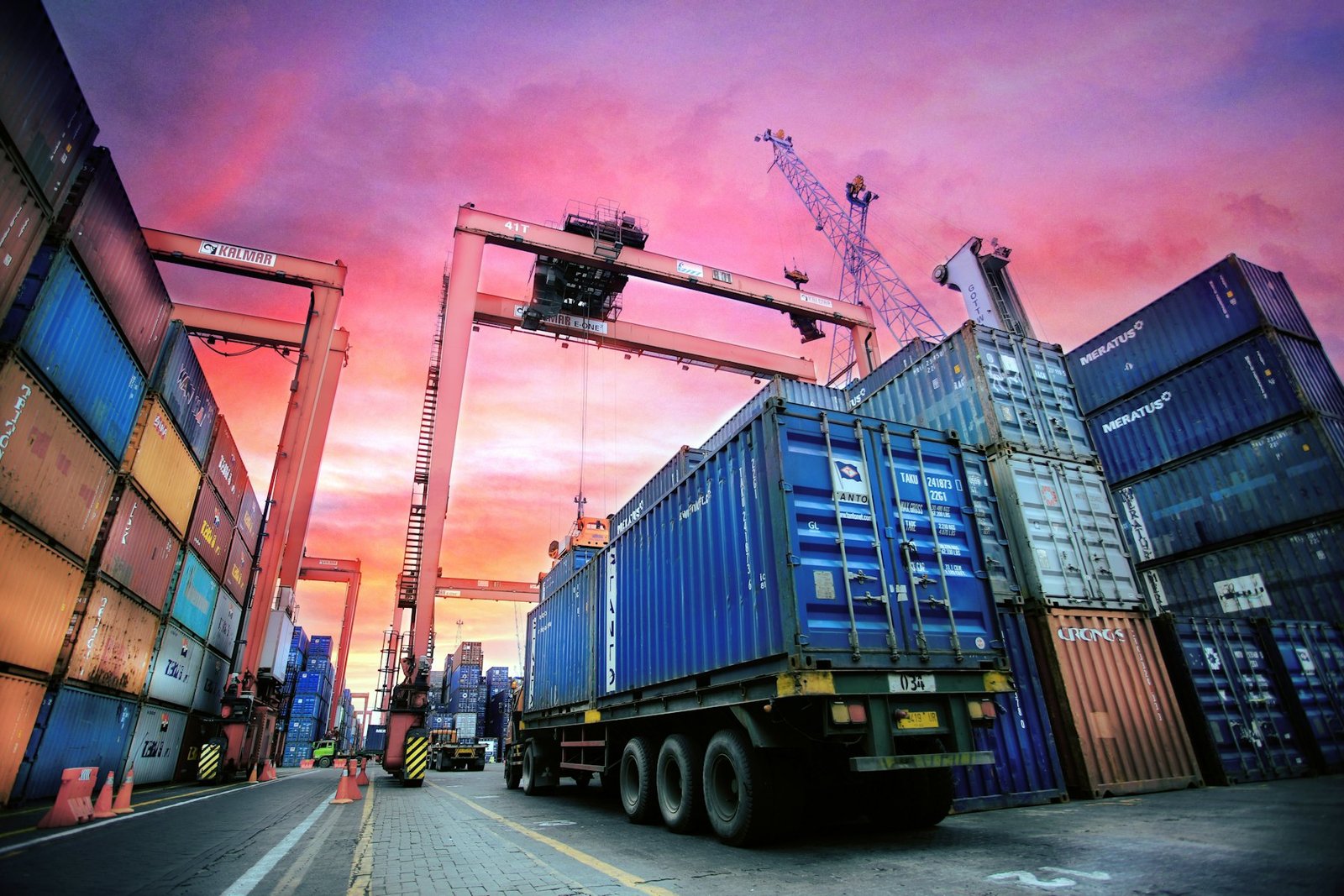 A shipping container being lifted onto a truck chassis at a container terminal at dusk